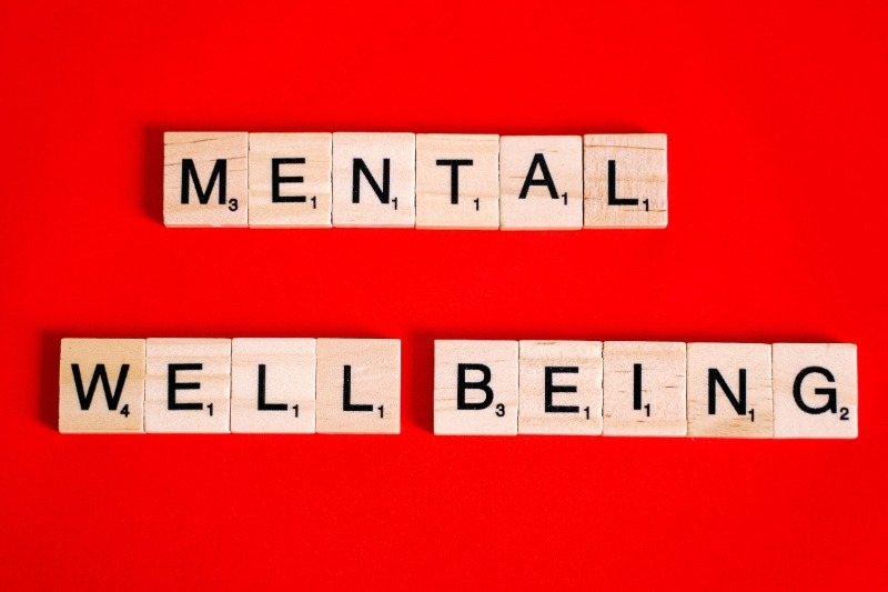 Scrabble game tiles saying Mental Well Being on a bright red backgroung.